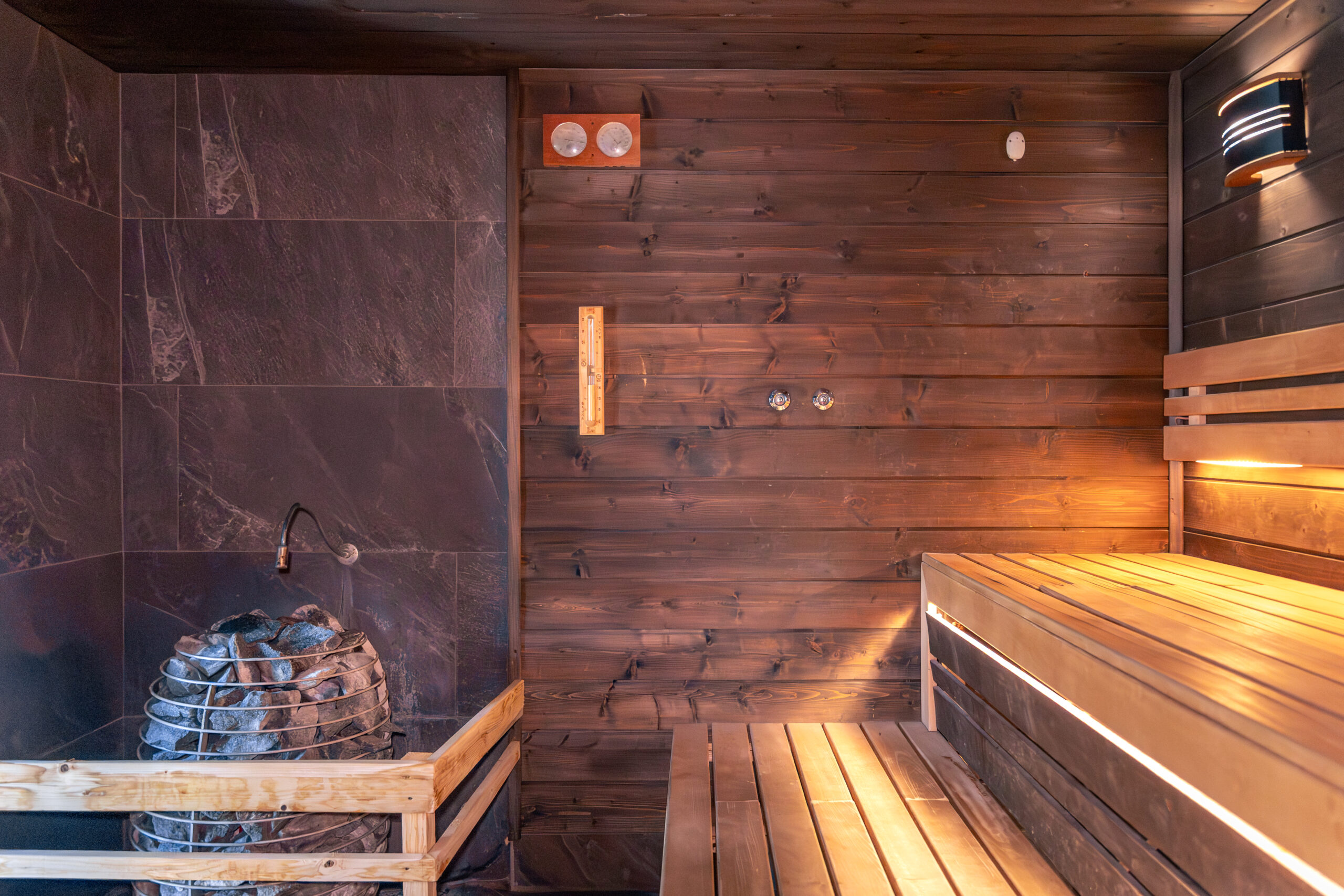 sauna with stones thermometer warm benches light nordic wellness scaled TheHomeQuality